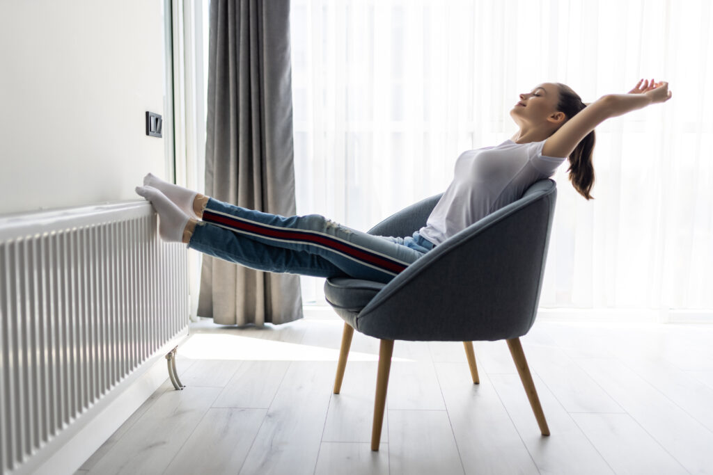 A woman relaxing in a comfortable chair by a large window in a bright, sunlit high-rise apartment.