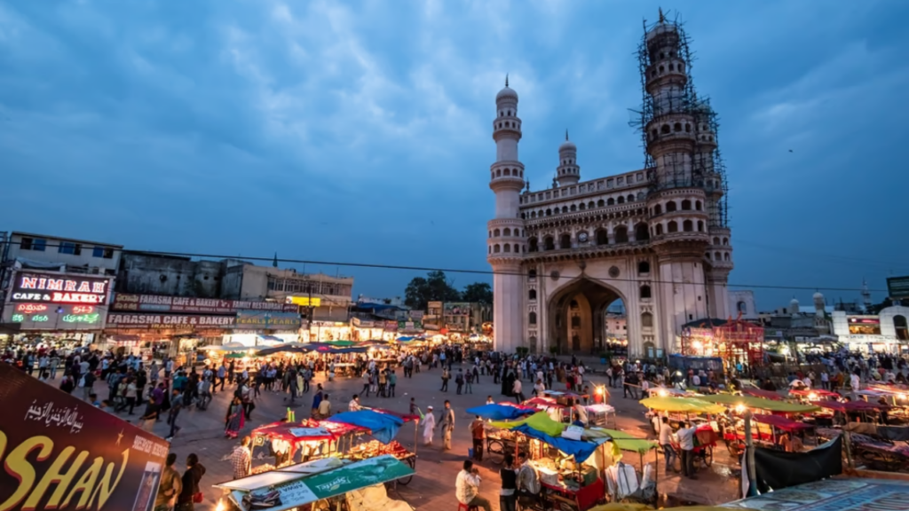A view of the historical Charminar monument in Hyderabad, taken from a busy street during early morning, with power lines crossing in front of the white structure.