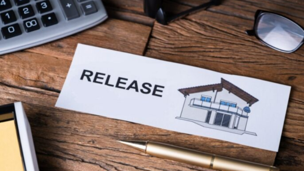 A white card with the word "RELEASE" and a simple house illustration sits on a wooden desk. A gold pen, a calculator, and eyeglasses are visible in the background.