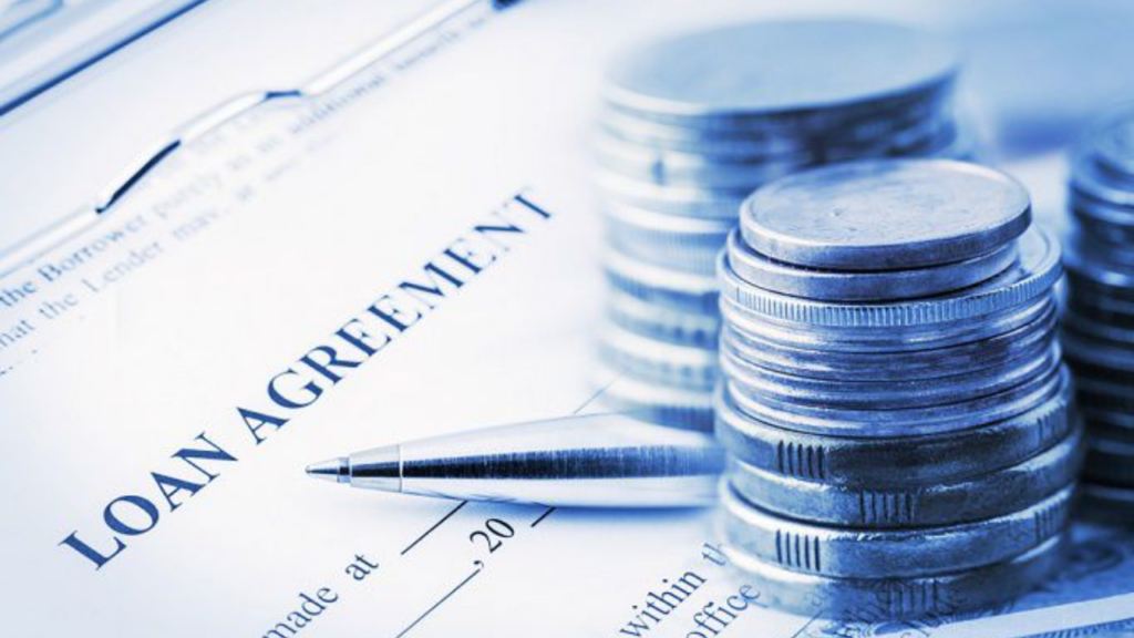 A silver pen resting on a loan agreement document next to stacks of coins.